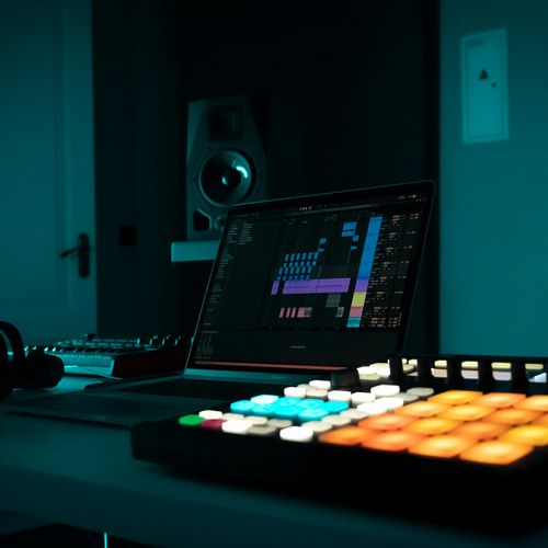 Home music studio in a room with dim lighting. Studio includes a laptop, headphones, speakers, and musical equiment.